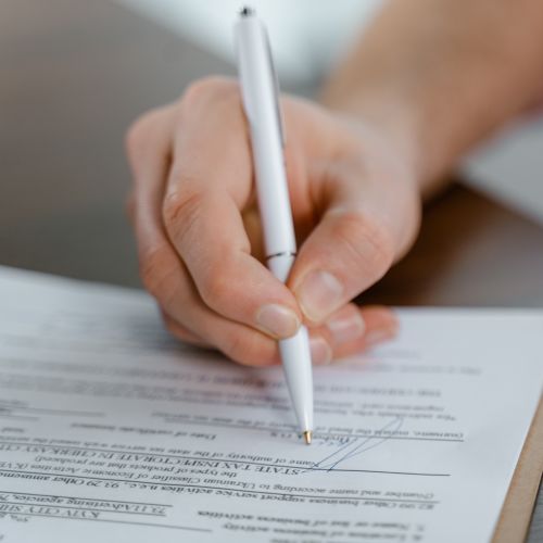 Detailed view of a hand writing a signature on an official document with a ballpoint pen.